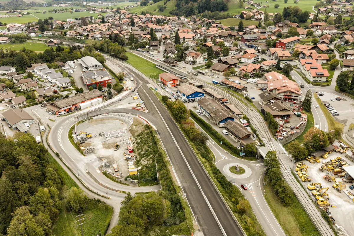 Luftaufnahme einer Baustelle an einer Straße in einer ländlichen Umgebung mit mehreren Wohn- und Gewerbegebäuden.