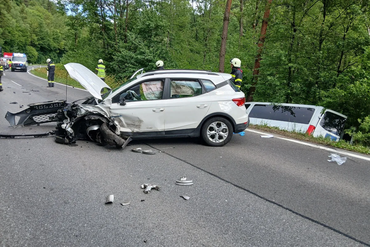 Ein stark beschädigtes weißes Auto steht auf einer Landstraße, umgeben von Trümmern. Im Hintergrund sind Rettungskräfte zu sehen, die die Unfallstelle sichern.
