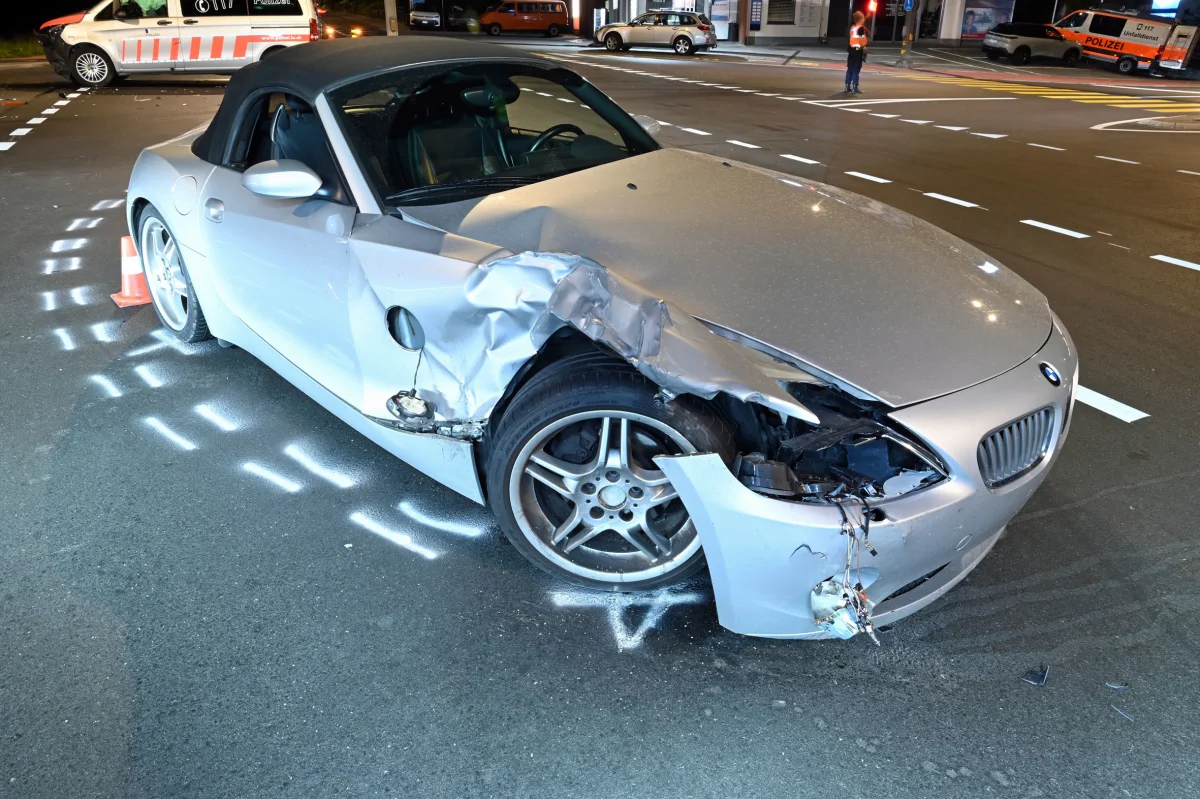Ein silberner BMW Roadster hat vorne rechts einen starken Unfallschaden. Im Hintergrund ist ein Polizeifahrzeug sichtbar.