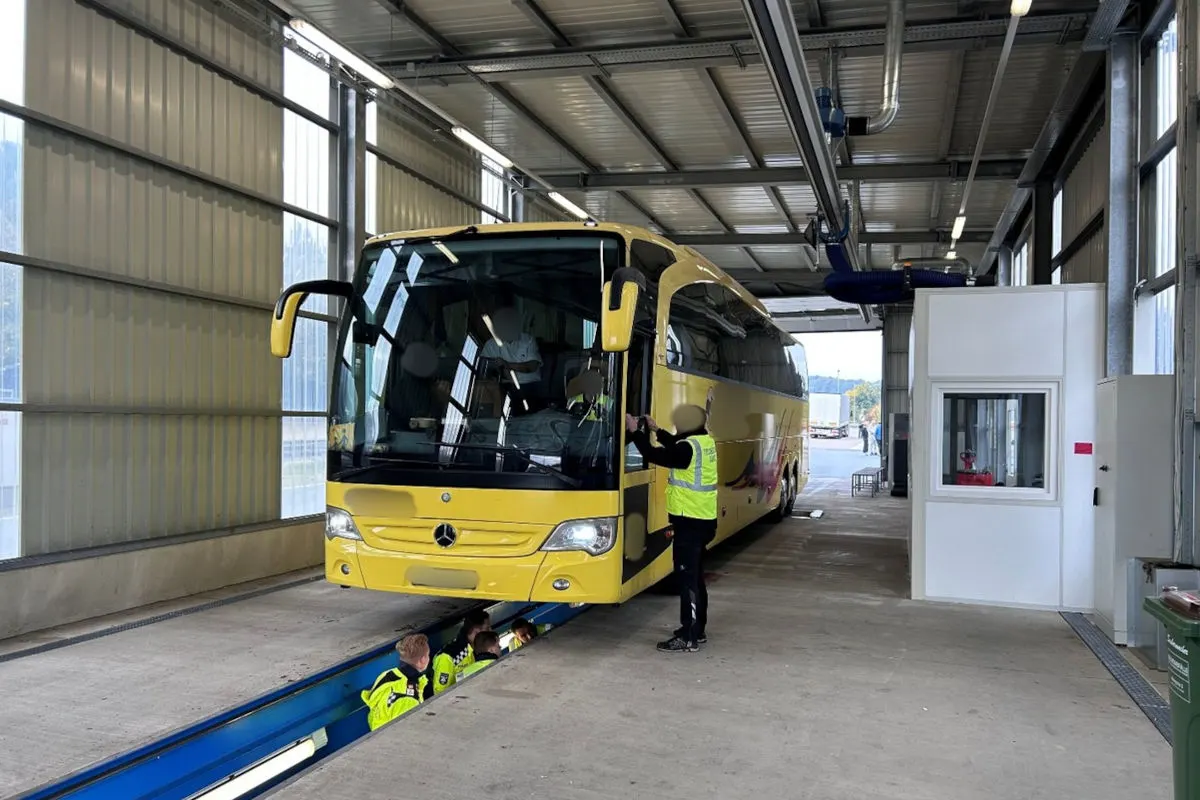 Ein gelber Reisebus steht in einer Halle auf einer Inspektionsstation, während mehrere Polizisten den Bus untersuchen.