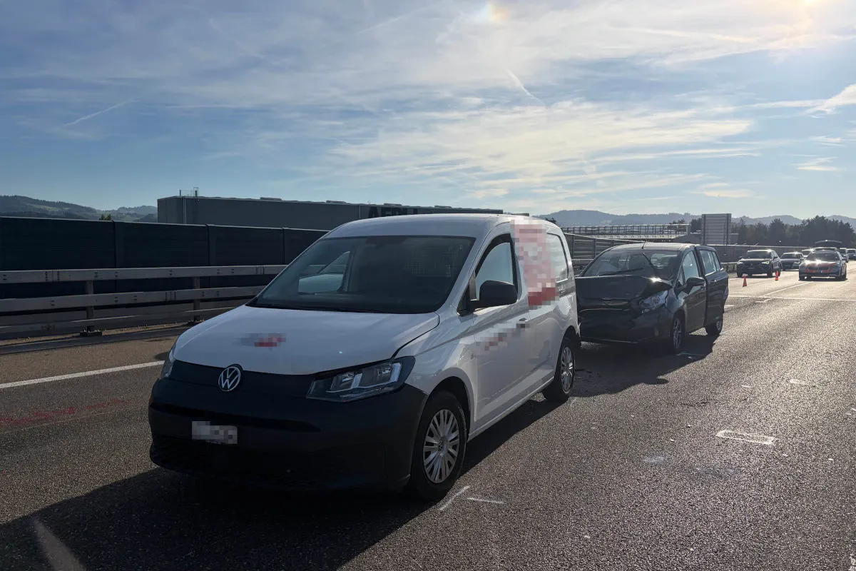 Ein weißer VW Transporter steht auf der Autobahn, dahinter ein beschädigtes schwarzes Auto. Die Szenerie wird von klarem Himmel und Sonnenschein begleitet.