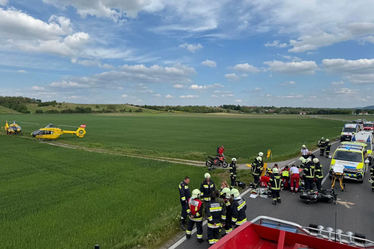 Eine Gruppe von Einsatzkräften steht auf einer Landstraße, begleitet von Rettungswagen und einem gelben Helikopter in einem Feld.
