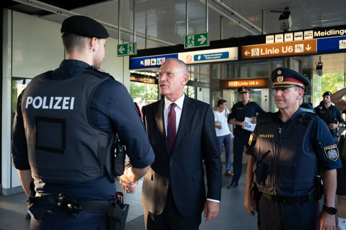 In einer Bahnhofshalle schüttelt ein Mann im Anzug einem Polizisten die Hand. Weitere Polizisten sind im Hintergrund zu sehen.