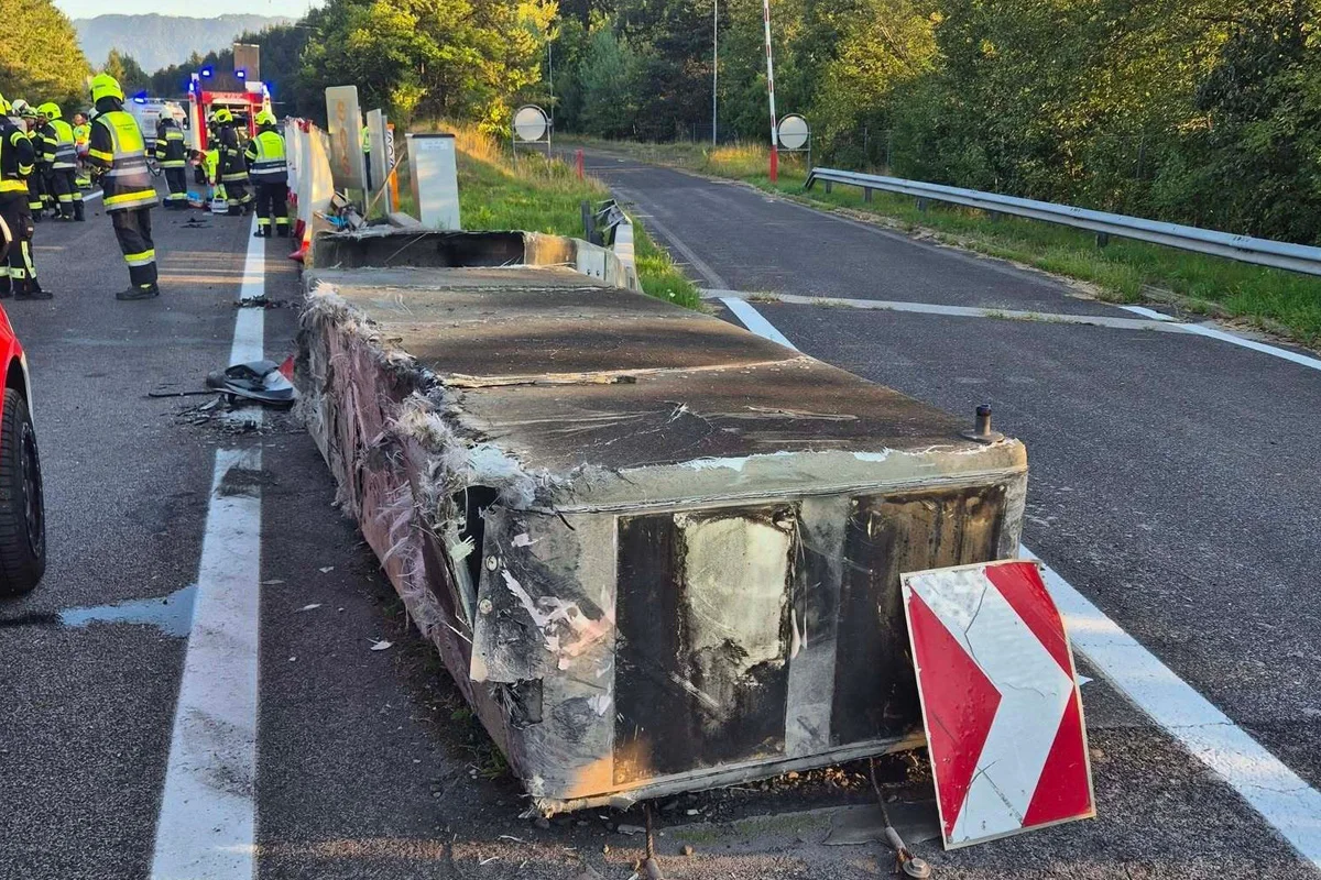 Eine beschädigte Betonbarriere liegt auf der Autobahn, umgeben von mehreren Feuerwehrleuten in gelben Helmen, die die Stelle sichern.