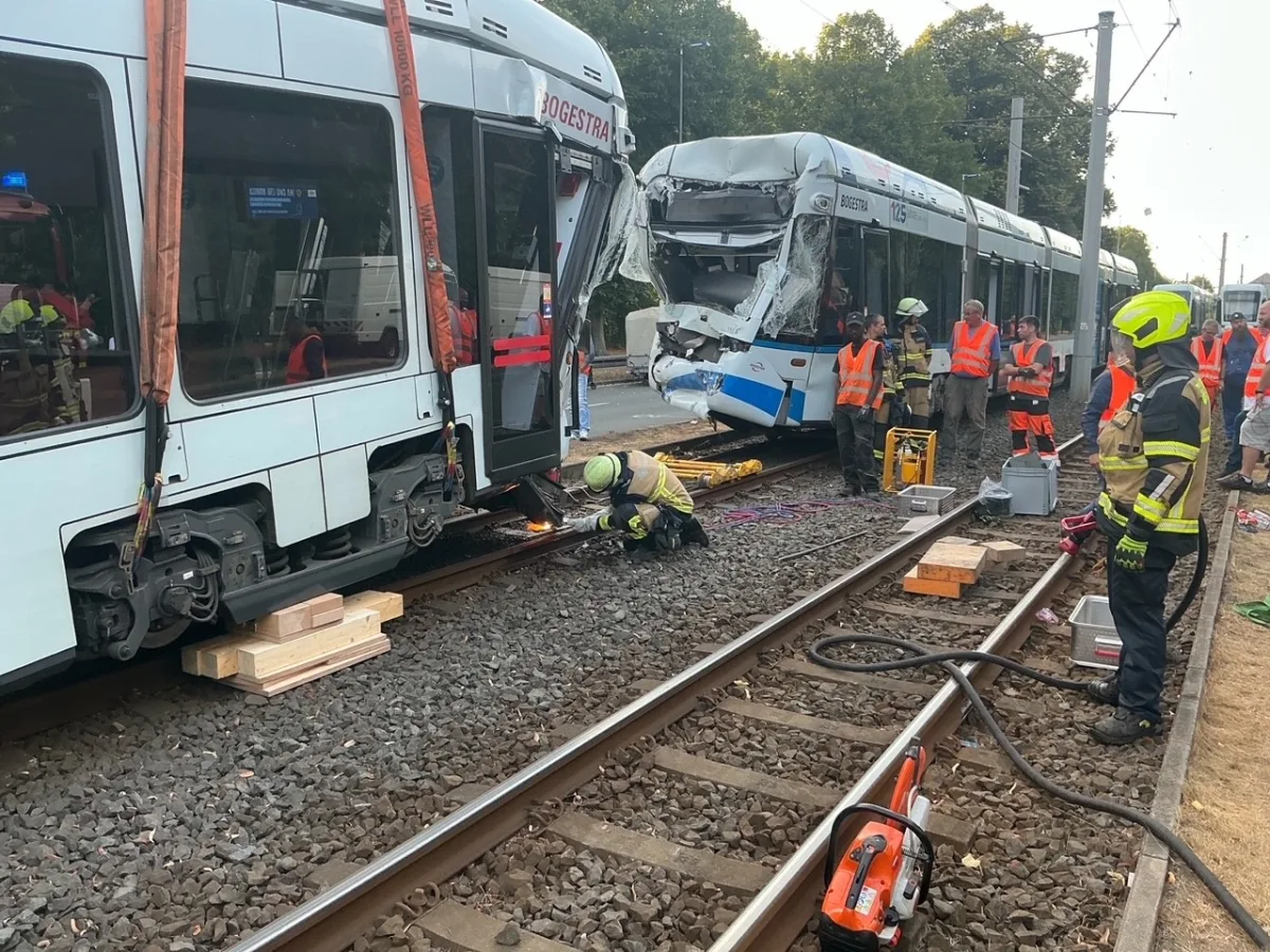 Zwei stark beschädigte Straßenbahnen stehen auf den Gleisen, umgeben von Einsatzkräften in orangefarbenen Westen und Helmen. Technische Geräte liegen auf dem Boden.