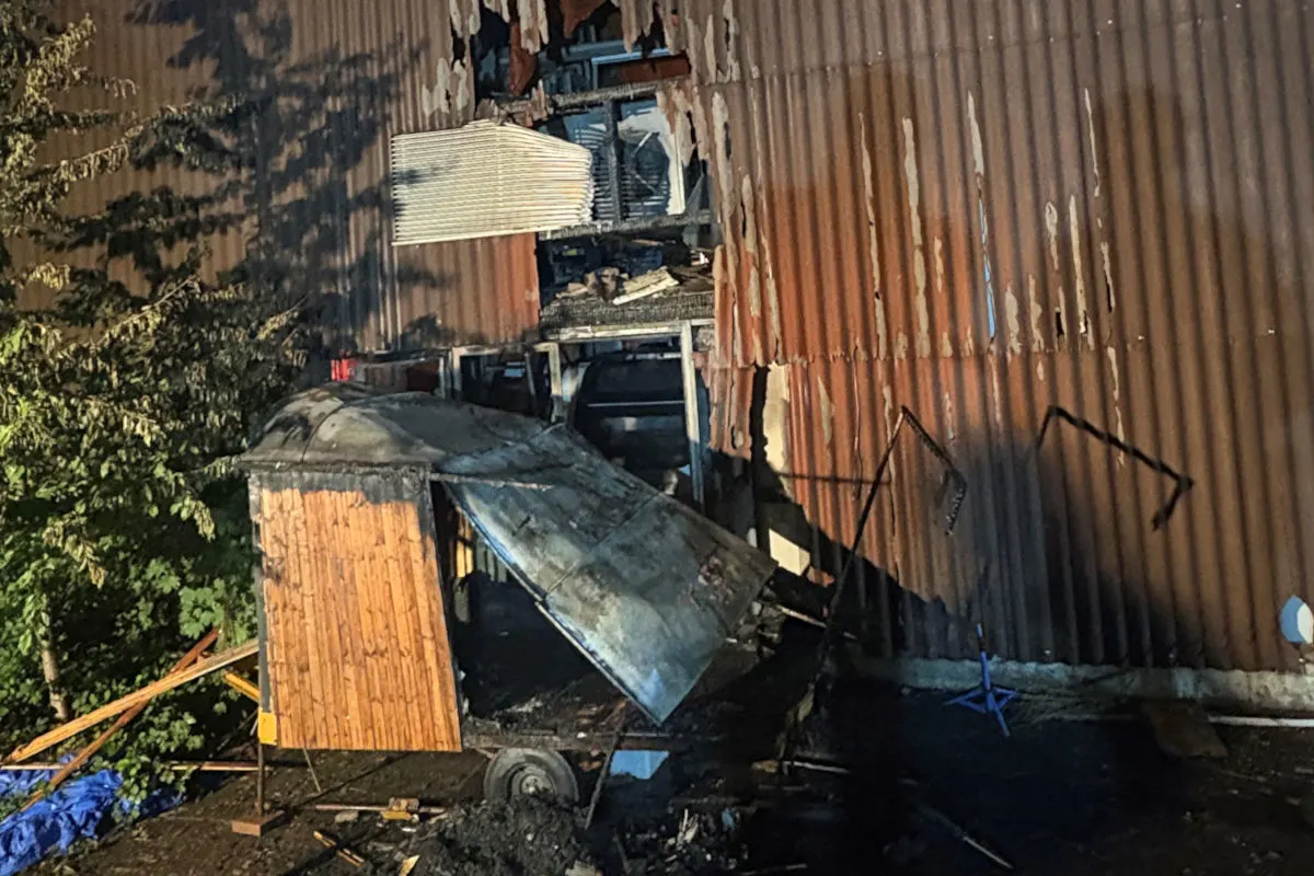 Die Fassade eines Gebäudes zeigt große Brandschäden mit verkohlten und zerstörten Strukturen. Ein Baum ist links im Bild.