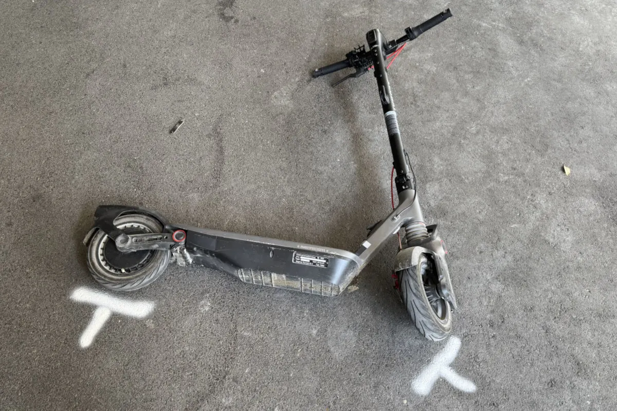 Ein beschädigter E-Scooter liegt quer auf einer asphaltierten Fläche. Umgeben von weißen Markierungen auf dem Boden.
