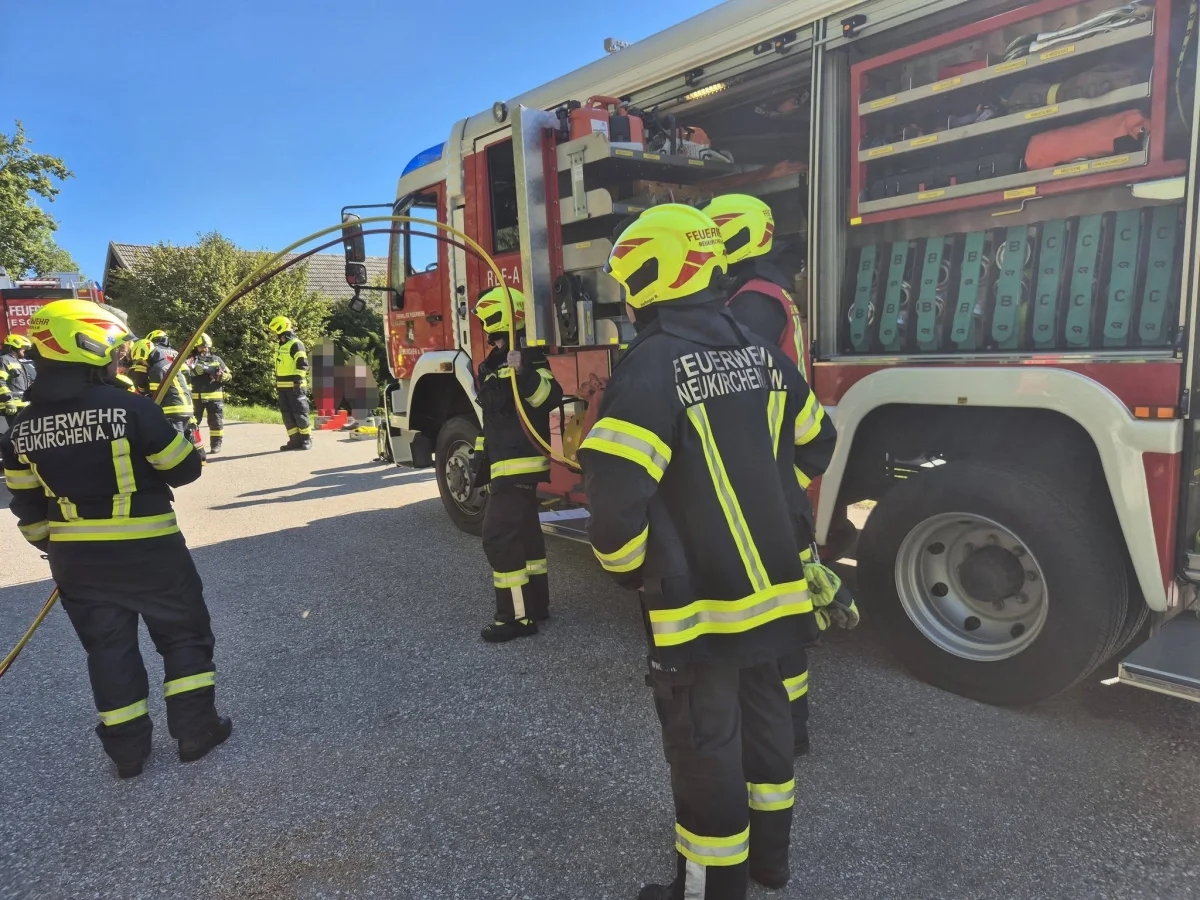 Mehrere Feuerwehrleute in Einsatzkleidung stehen nahe einem geöffneten Feuerwehrauto auf einer Straße.