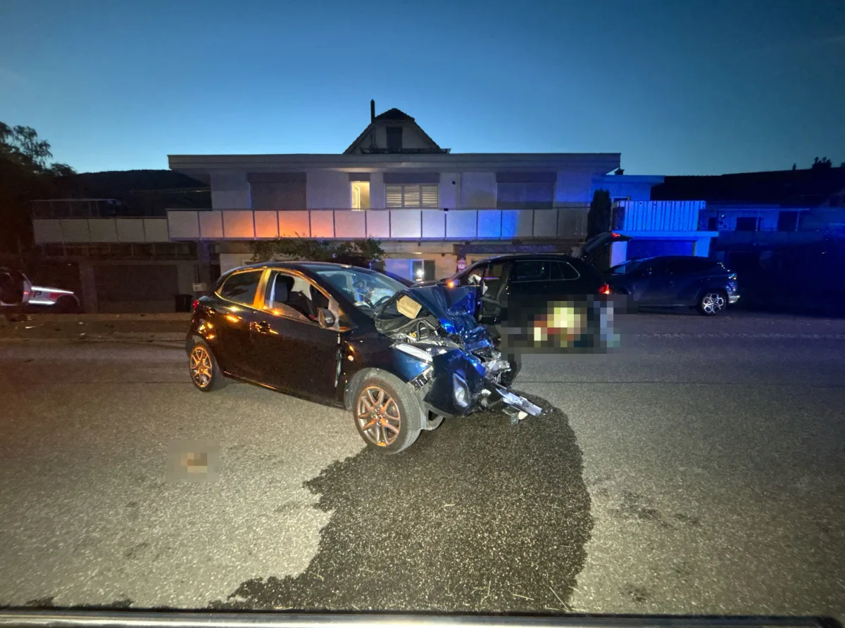 Ein Auto mit schweren Frontschäden steht auf einer Straße. Im Hintergrund sind Wohnhäuser bei Nacht zu sehen.