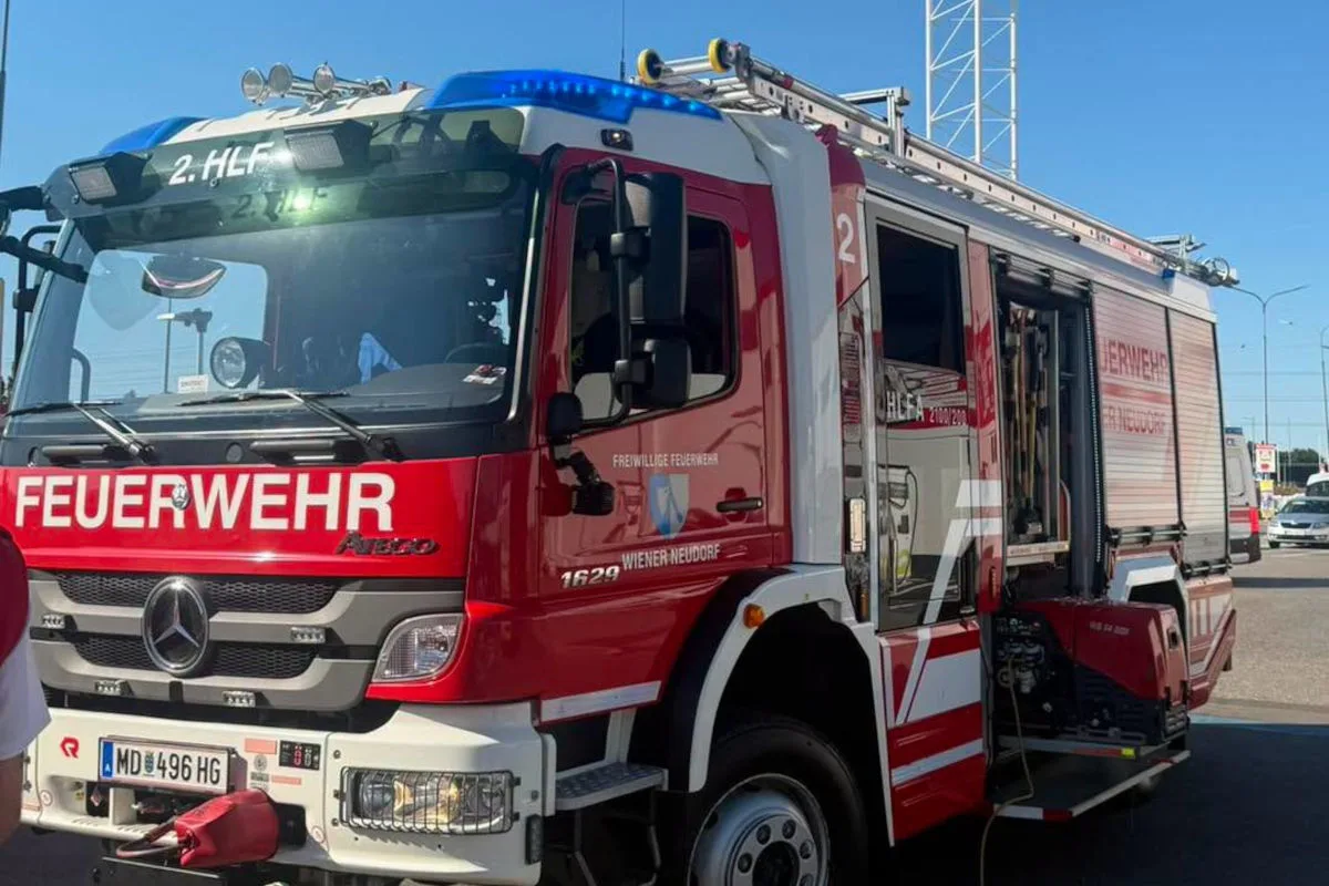 Ein rotes und weißes Feuerwehrfahrzeug der Marke Mercedes-Benz, markiert mit 'Freiwillige Feuerwehr Wiener Neudorf', steht auf einem Parkplatz bei Tageslicht.
