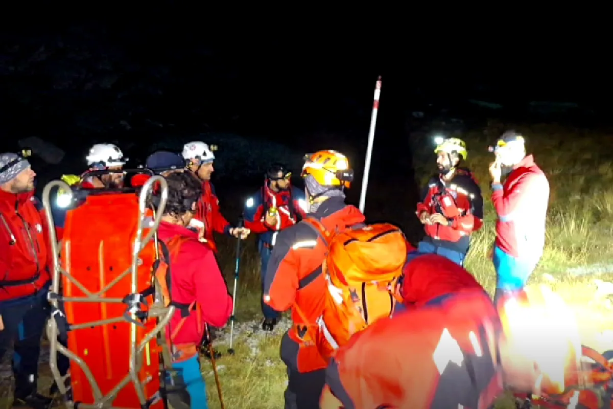 Mehrere Rettungskräfte in roter Einsatzkleidung stehen nachts auf einem Berg. Sie tragen Helme und Ausrüstungen.