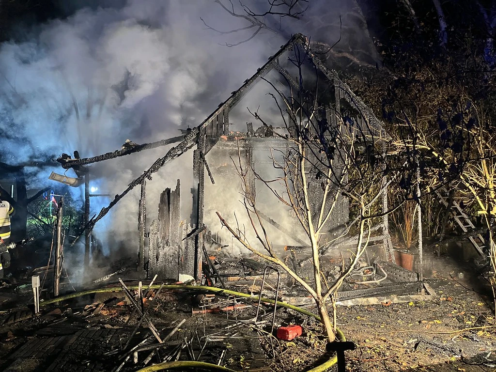 Ein kleines Gebäude ist vollständig niedergebrannt, Rauch steigt von den Überresten auf. Feuerwehrschläuche liegen am Boden.
