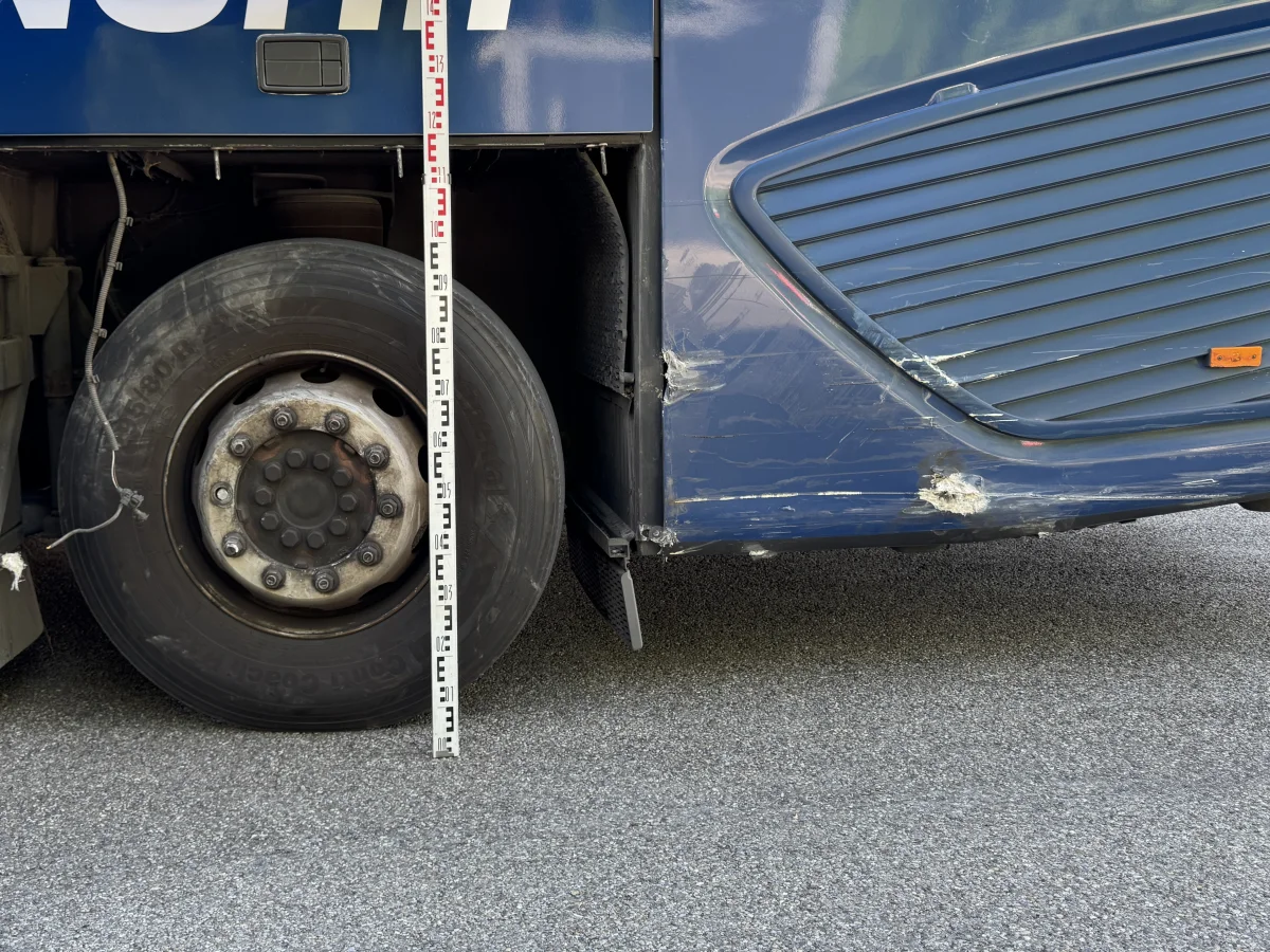 Ein Busreifen mit sichtbaren Beschädigungen an der Radkappe und dem umliegenden Bereich. Eine Messlatte steht senkrecht daneben, um den Schadensumfang zu verdeutlichen.