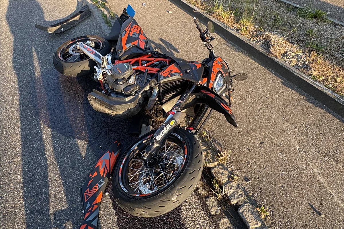 Ein beschädigtes Motorrad liegt auf dem Boden, wobei Teile auf der Straße verstreut sind. Die Szene ist bei Tageslicht fotografiert.