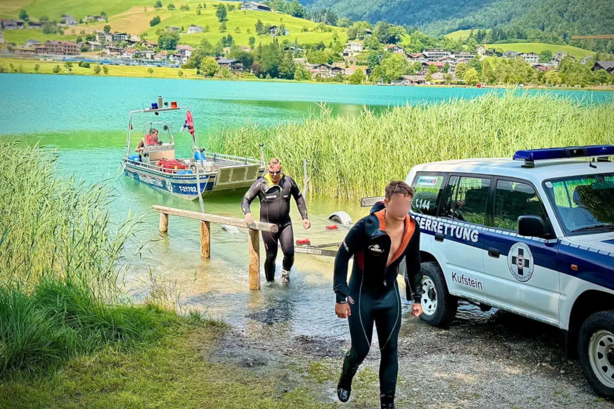 Zwei Männer in Tauchanzügen verlassen den Thiersee. Ein Rettungsfahrzeug der Wasserrettung Kufstein steht am Ufer.