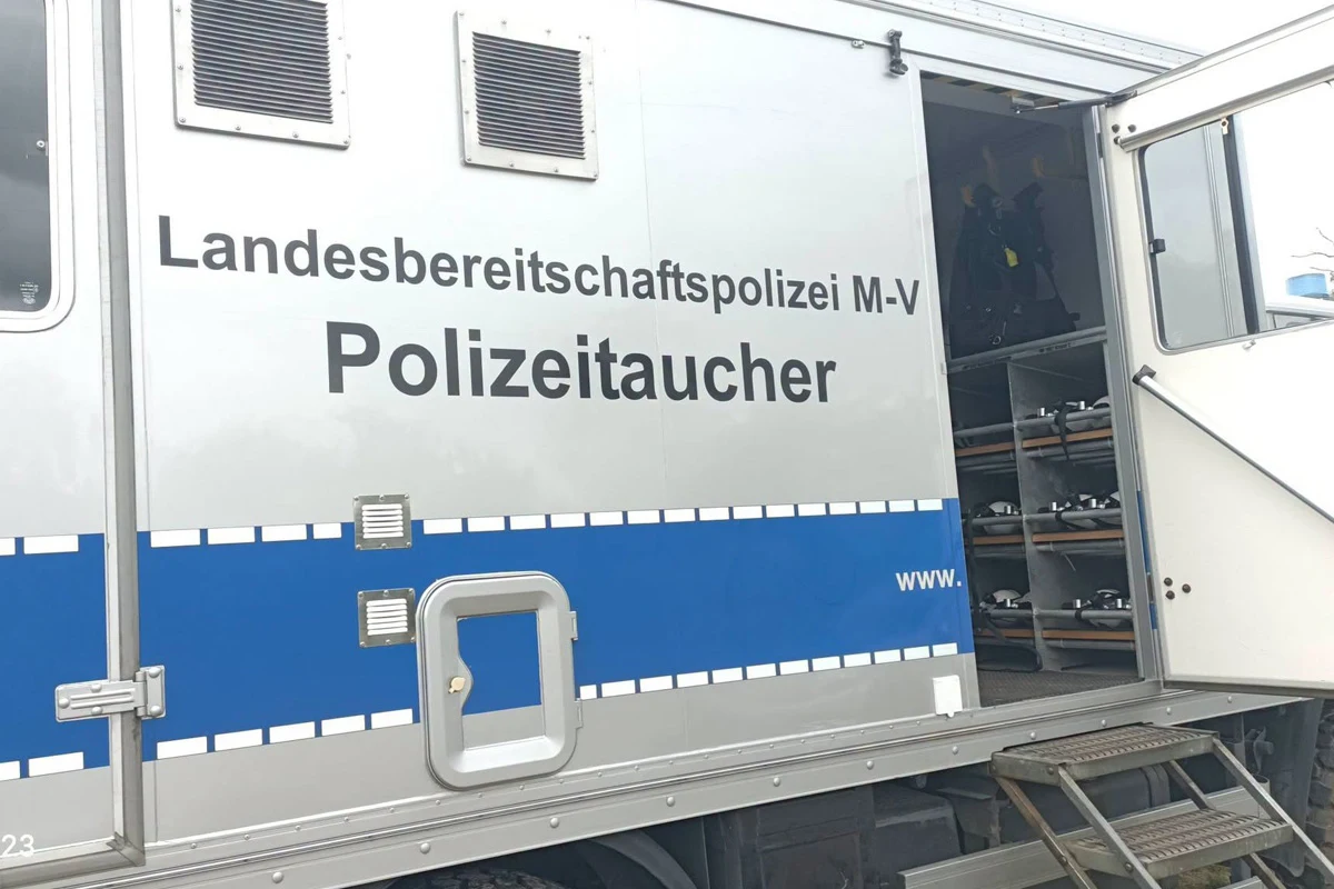 Das Bild zeigt die Seitenansicht eines Fahrzeugs der Landesbereitschaftspolizei M-V mit der Aufschrift 'Polizeitaucher' auf der Tür. Die Tür steht offen.