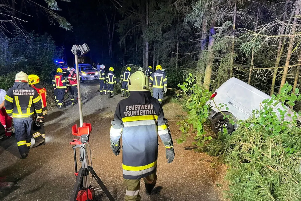 Mehrere Feuerwehrleute sind im Einsatz, nachdem ein weißes Fahrzeug im Wald von der Straße abgekommen ist.