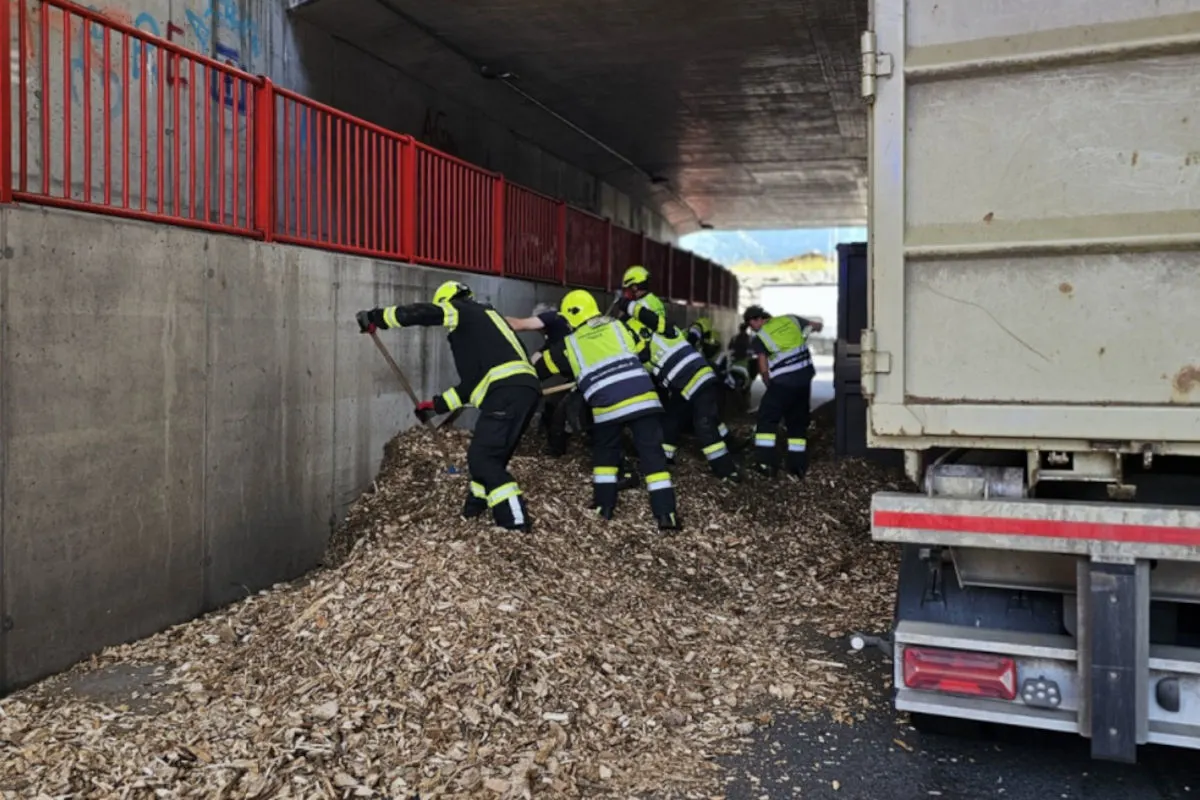 Mehrere Feuerwehrleute in Schutzkleidung räumen Holzspäne in einer Unterführung, neben einem geparkten Lastwagen.