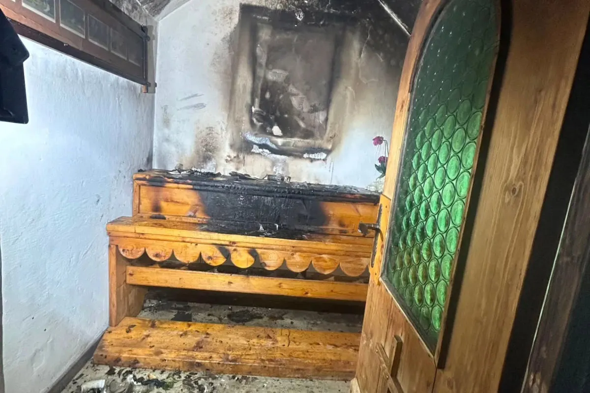 In einer kleinen Kapelle ist ein Holzaltar sichtbar, der durch ein Feuer stark beschädigt wurde. Die Wand dahinter ist ebenfalls verkohlt.