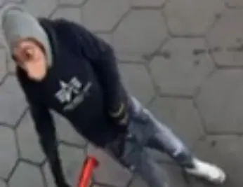 Eine Person, bekleidet mit grauem Hoodie und Jeans, steht auf einem dunklen Pflasterboden und schaut in die Kamera.