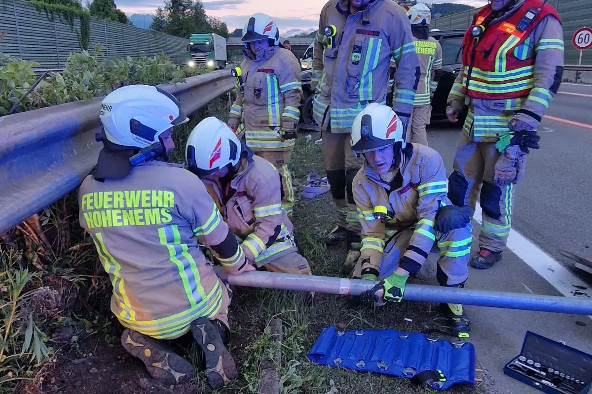Mehrere Feuerwehrleute sind an einer Autobahnleitplanke beschäftigt. Sie tragen Schutzanzüge mit Helm.