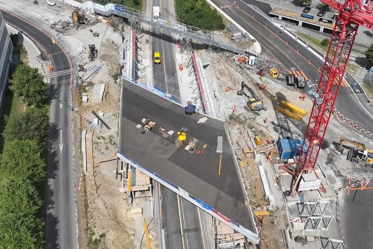 Die Luftaufnahme zeigt eine große Baustelle mit einem unfertigen Straßenabschnitt, mehreren Baugeräten und einem roten Baukran.