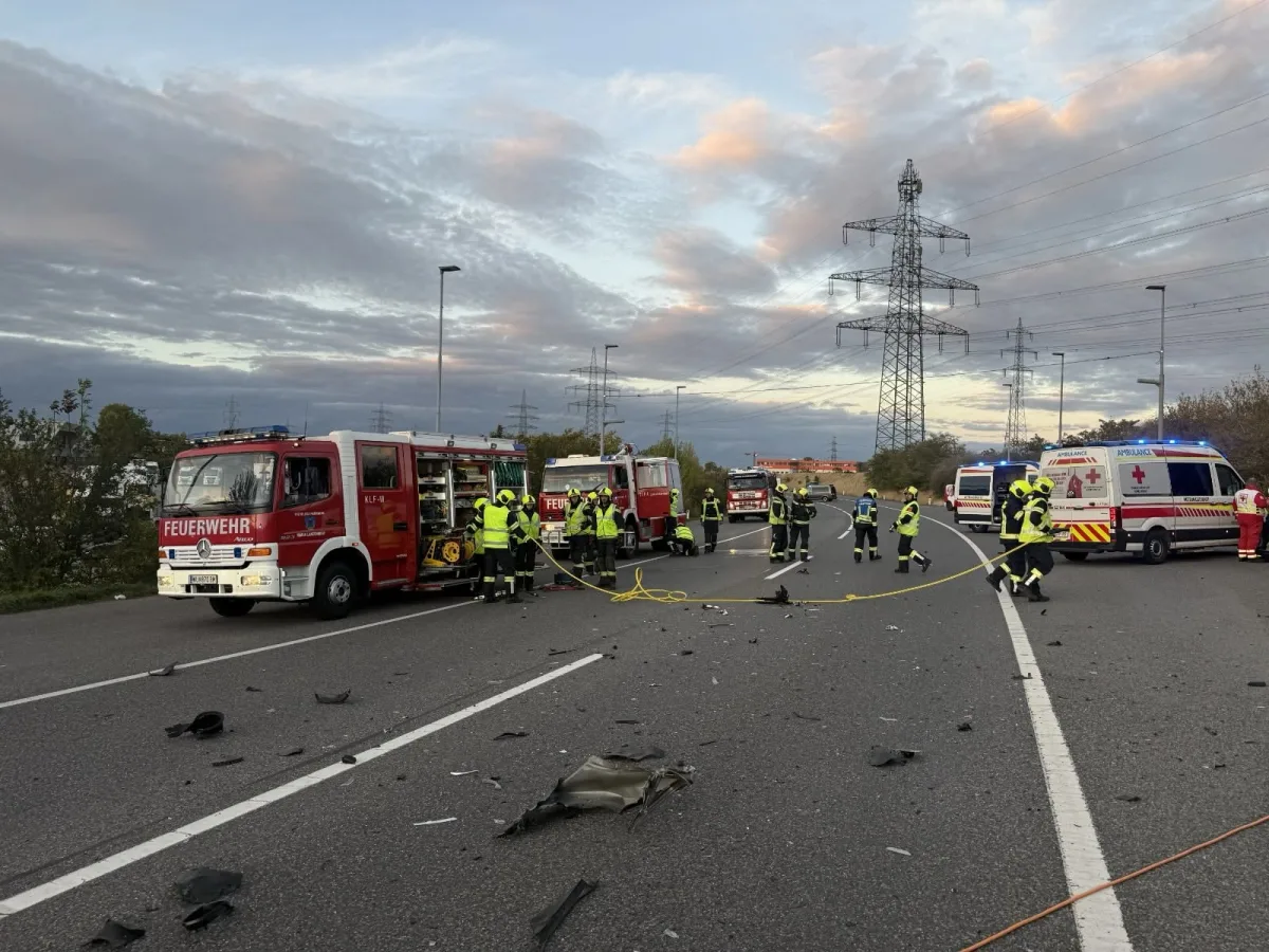 Mehrere Feuerwehrfahrzeuge und Rettungswagen stehen auf einer Autobahn, umgeben von Trümmerteilen und Einsatzkräften bei Abenddämmerung.