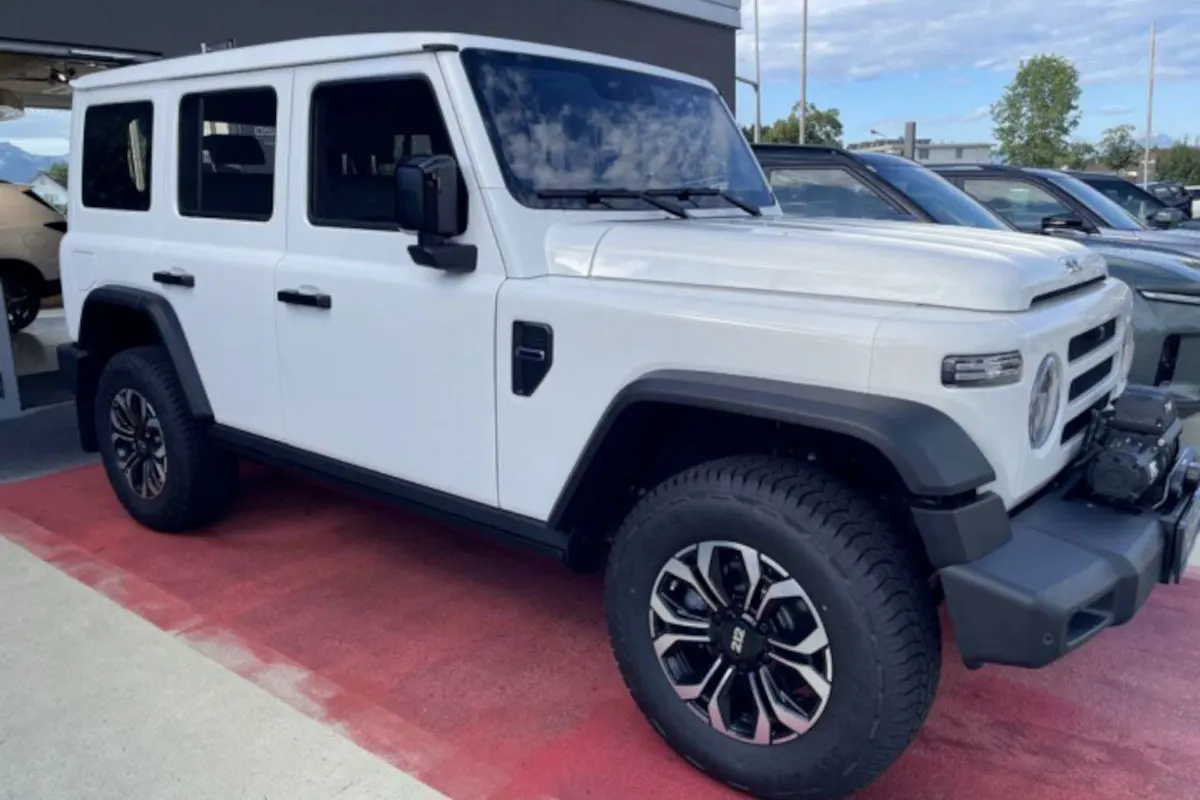 Ein weißer Geländewagen steht auf einem roten Bodenbelag in einem Autohaus. Im Hintergrund sind weitere Fahrzeuge sichtbar.