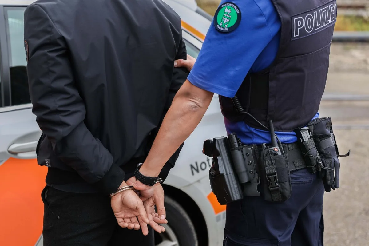 Ein Polizist der Kantonspolizei St. Gallen legt einer Person vor einem Einsatzfahrzeug Handschellen an. Es ist Tag und die Szene ist im Freien.