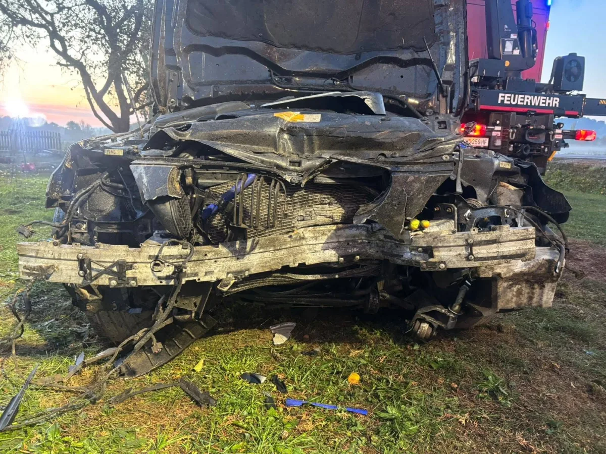 Die Vorderseite eines Lkws ist stark beschädigt nach einem Unfall. Im Hintergrund ist ein Feuerwehrauto zu sehen.