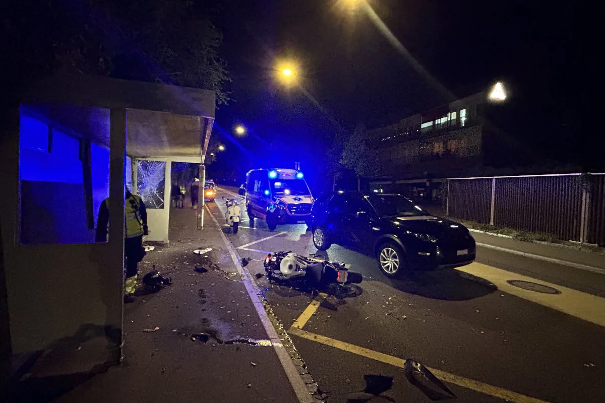 Eine nächtliche Unfallstelle zeigt einen gestürzten Motorroller und ein Rettungsfahrzeug mit Blaulicht. Zwei Pkw sind ebenfalls auf der Straße sichtbar.