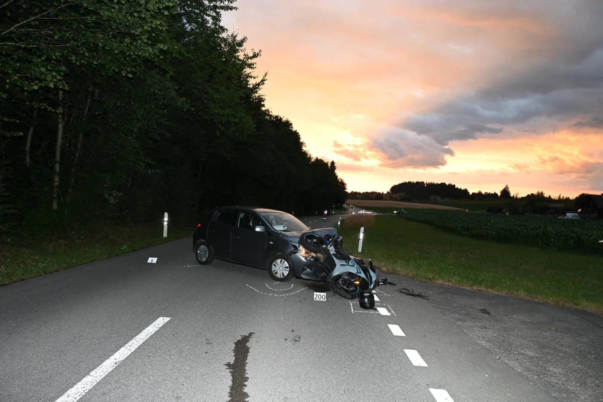 Ein dunkles Auto und ein gestürztes Motorrad kollidiert auf einer Landstraße in einer ländlichen Umgebung bei Abenddämmerung.
