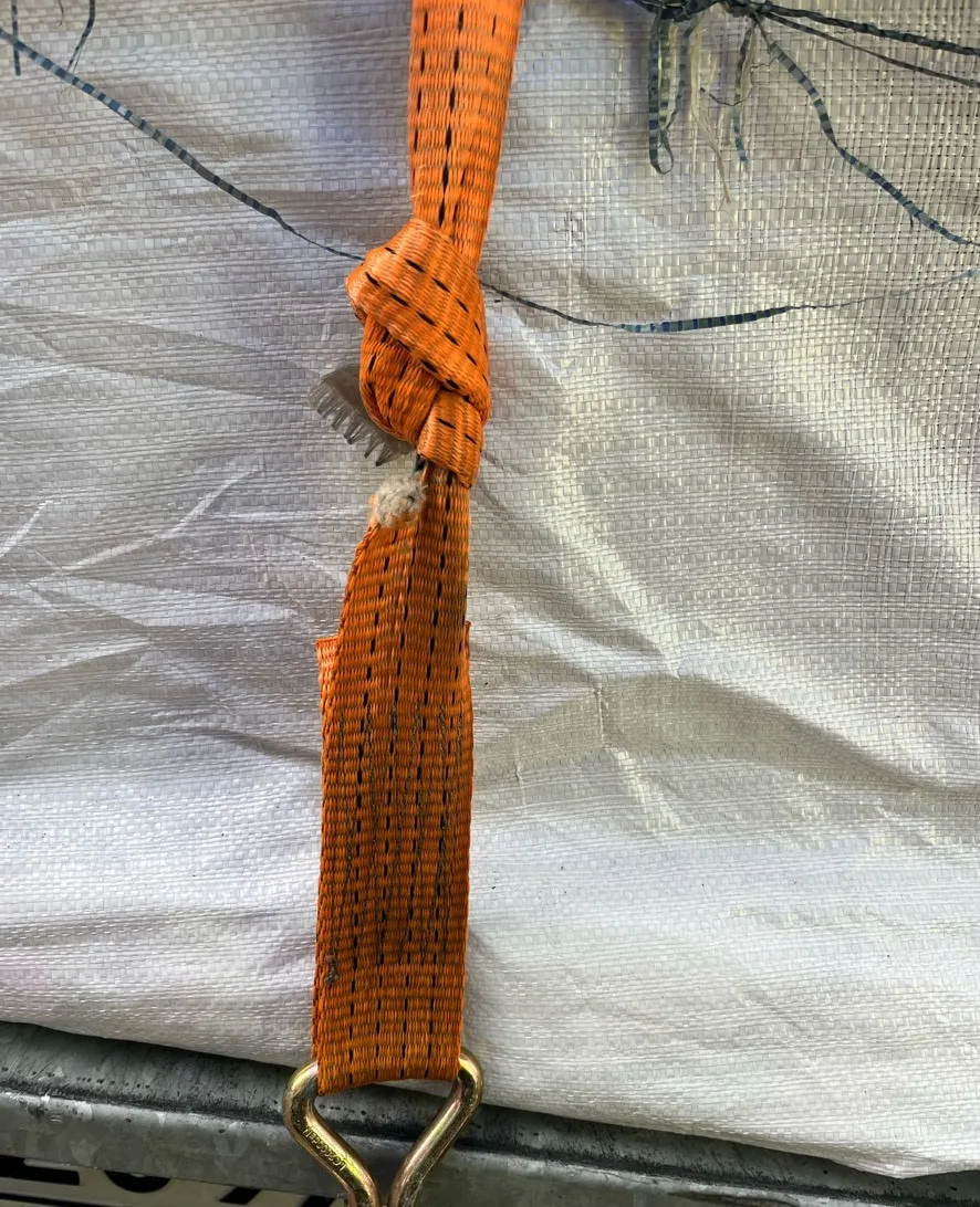 Ein orangefarbener Gurt zeigt deutlichen Abrieb neben einer befestigten Plane. Der Zustand des Gurts könnte auf unsachgemäße Anwendung hinweisen.