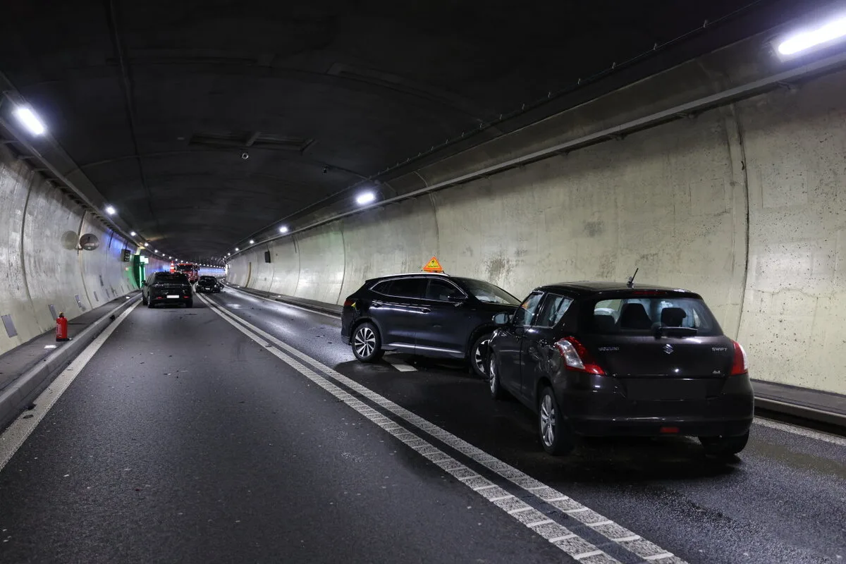 Zwei dunkle Fahrzeuge sind in einem Unfall in einer Tunnelröhre verwickelt. Eines der Autos hat ein Warndreieck auf dem Dach.