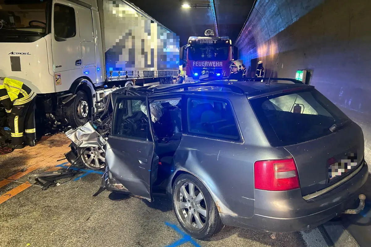 Ein schwer beschädigter Pkw steht vor einem Lkw in einem Tunnel, umgeben von Einsatzkräften der Feuerwehr.