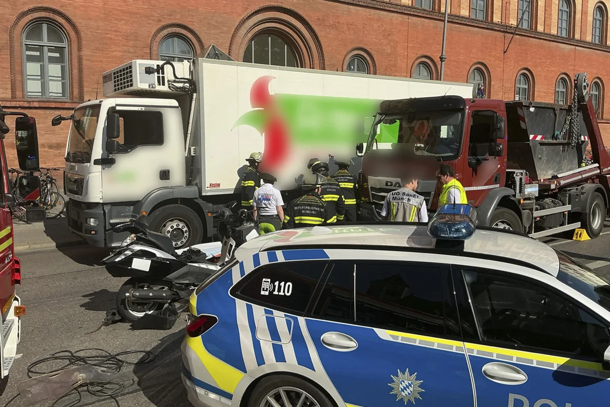 Ein Unfall zwischen einem weißen Lkw, einem roten Lkw und einem Polizeifahrzeug in einer Stadtstraße. Mehrere Einsatzkräfte sind vor Ort.