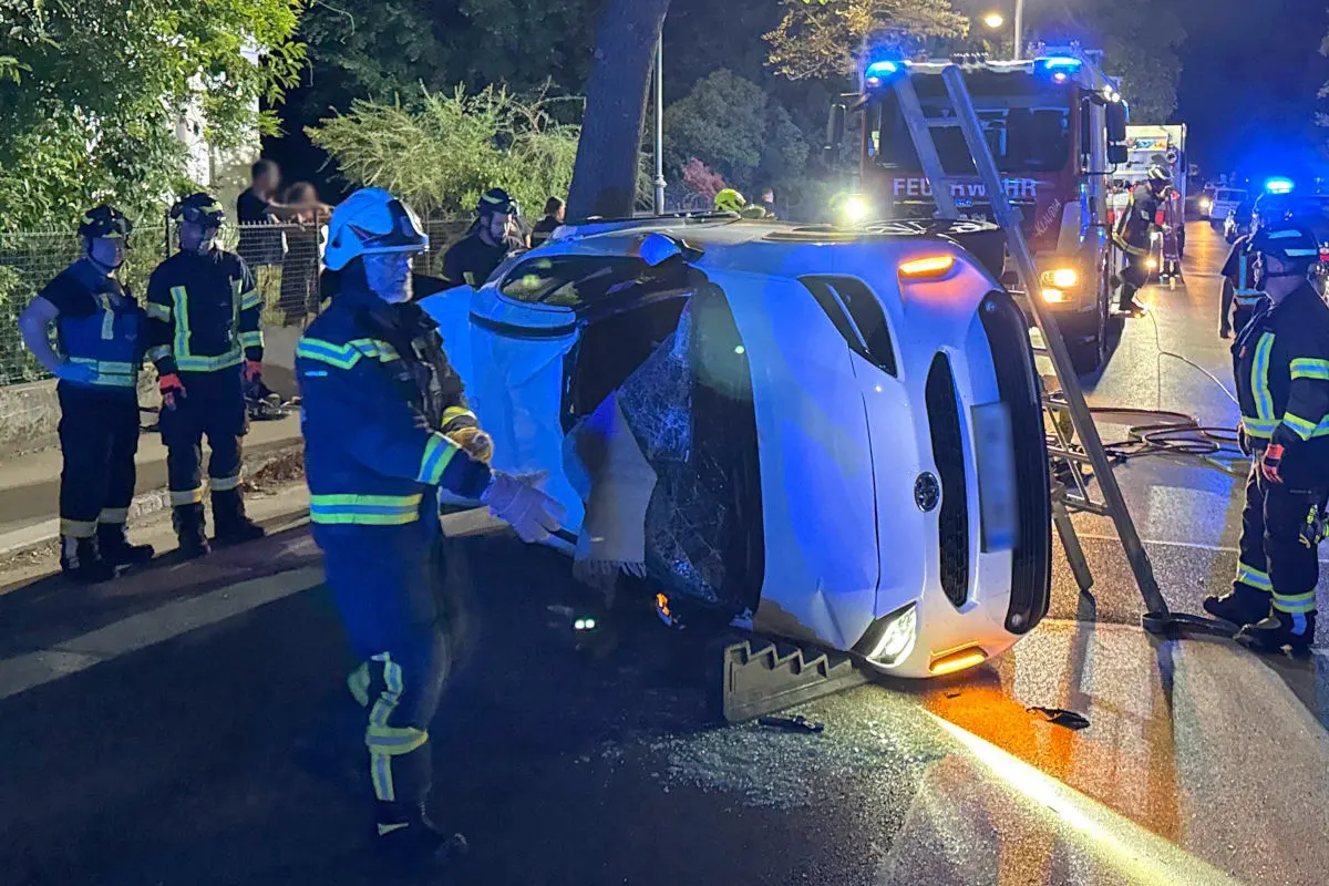 Das Bild zeigt Feuerwehrkräfte um ein auf der Seite liegendes, beschädigtes Auto bei nächtlichen Lichtverhältnissen.