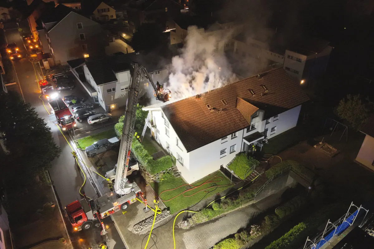 Im Einsatz bei Nacht löschen Feuerwehrleute mit einem Leiterwagen einen brennenden Dachstuhl eines Wohnhauses.