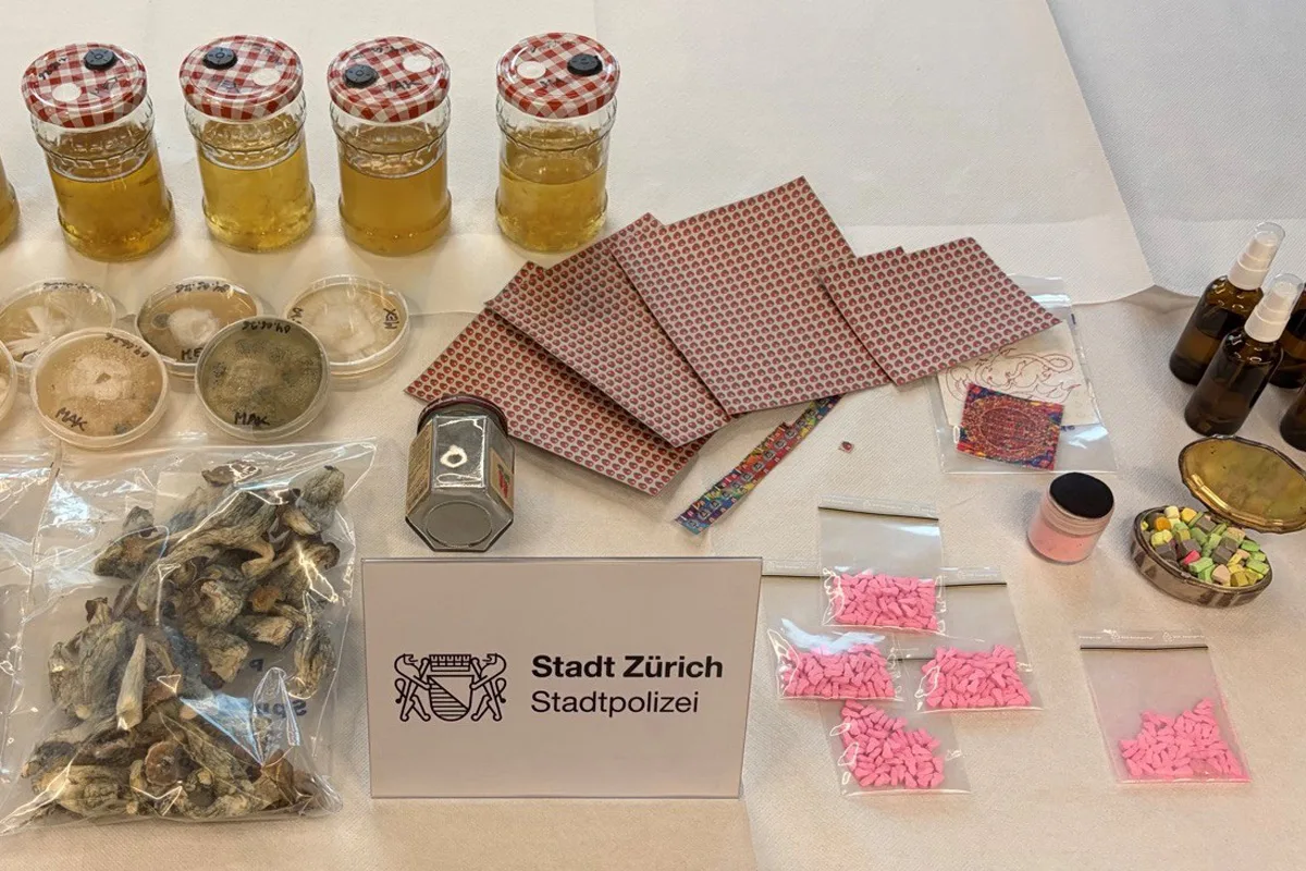 Auf einem Tisch liegen verschiedene Drogen wie Pillen und Pilze, daneben ein Schild der Stadtpolizei Zürich.
