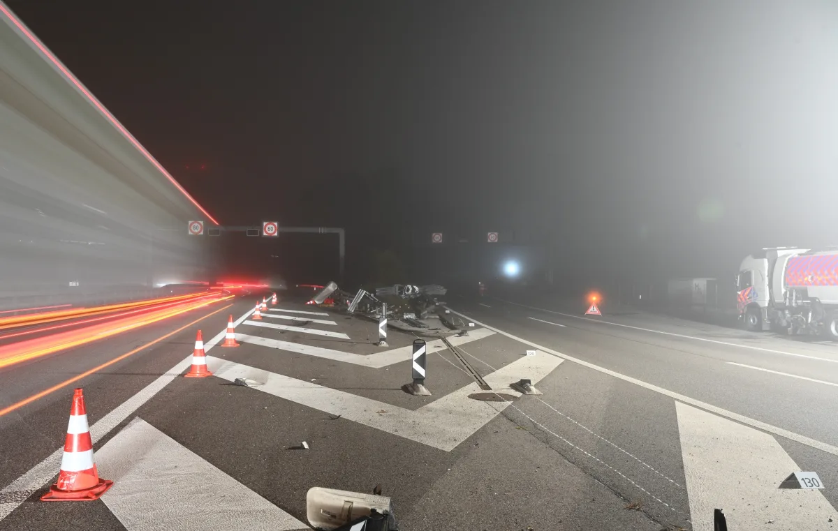 Auf einer nebligen Autobahn sind Straßentrümmer verteilt, Verkehrsleitkegel und ein beleuchteter Lkw sichtbar.