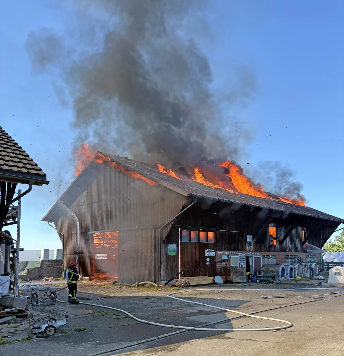 Eine Scheune steht in voller Ausdehnung in Flammen. Ein Feuerwehrmann löscht die Flammen von der Seite.