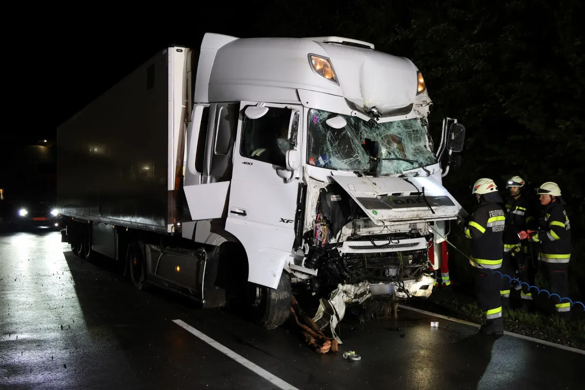 Ein weißer Lkw mit stark beschädigter Front steht nachts auf einer Straße. Mehrere Feuerwehrleute sind bei der Unfallstelle anwesend.