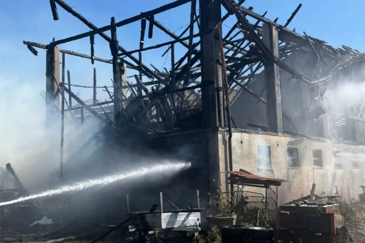 Ein stark beschädigtes Gebäude nach einem Brand, mit Rauchentwicklung und aktiven Löscharbeiten vor Ort.