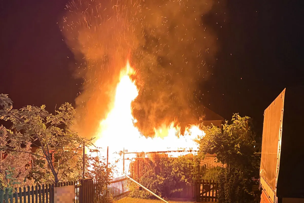 Bei Nacht brennt ein großes Feuer mit heftigem Flammen- und Funkenflug. Umgeben von Bäumen und einem Zaun.