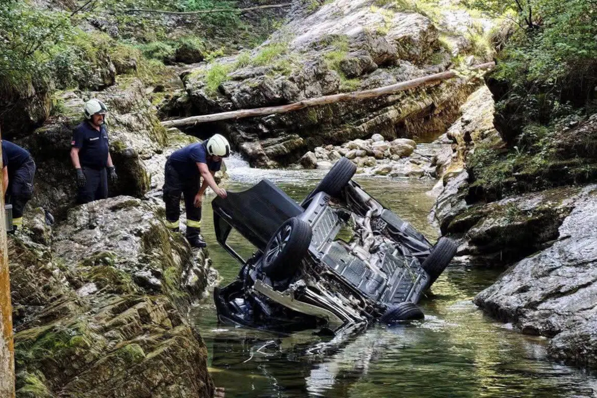 Ein umgedrehtes Auto liegt in einem flachen Bachbett umgeben von steiniger Natur. Mehrere Feuerwehrmänner sind zur Untersuchung anwesend.