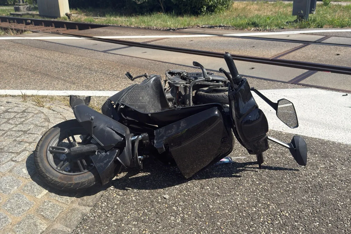 Ein gestürztes schwarzes Motorrad ist neben einer Bahngleiskreuzung zu sehen. Teile des Fahrzeugs sind sichtbar beschädigt.