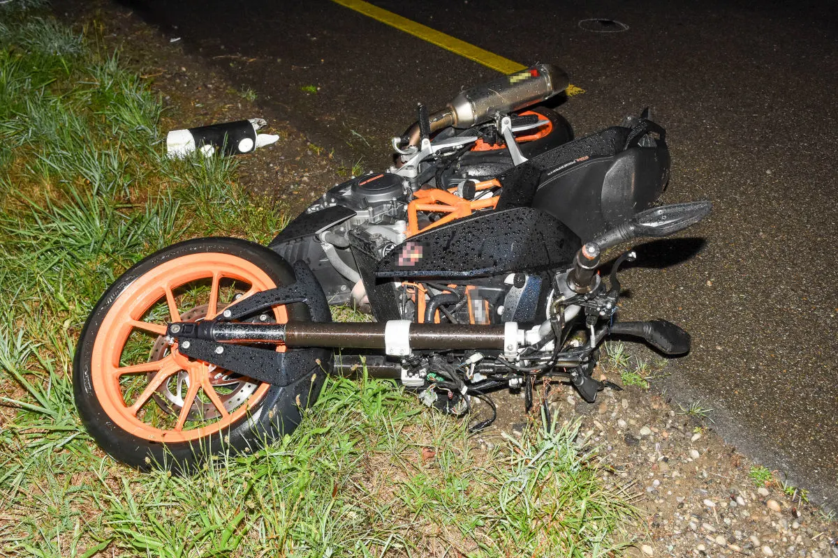 Ein Motorrad mit orangenen Felgen liegt im Gras, das bei regnerischen Bedingungen gestürzt ist. Teile des Motorrads liegen verstreut im Straßengraben.