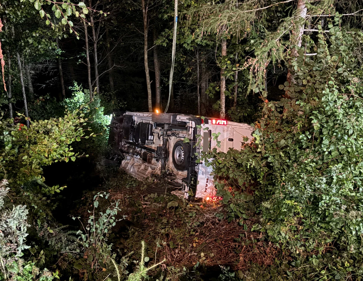 Ein Fahrzeug ist im Wald umgestürzt und liegt auf der Seite, nachts, mit hellem Licht beleuchtet.