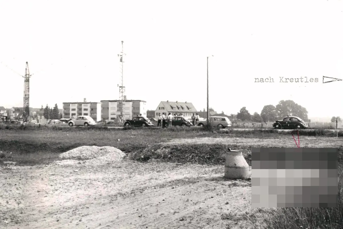 Eine historische Aufnahme zeigt mehrere Fahrzeuge und Menschen auf einer Baustelle in der Nähe von Kreutles. Im Hintergrund sind Kräne und Gebäude sichtbar, im Vordergrund liegt Bauschutt.