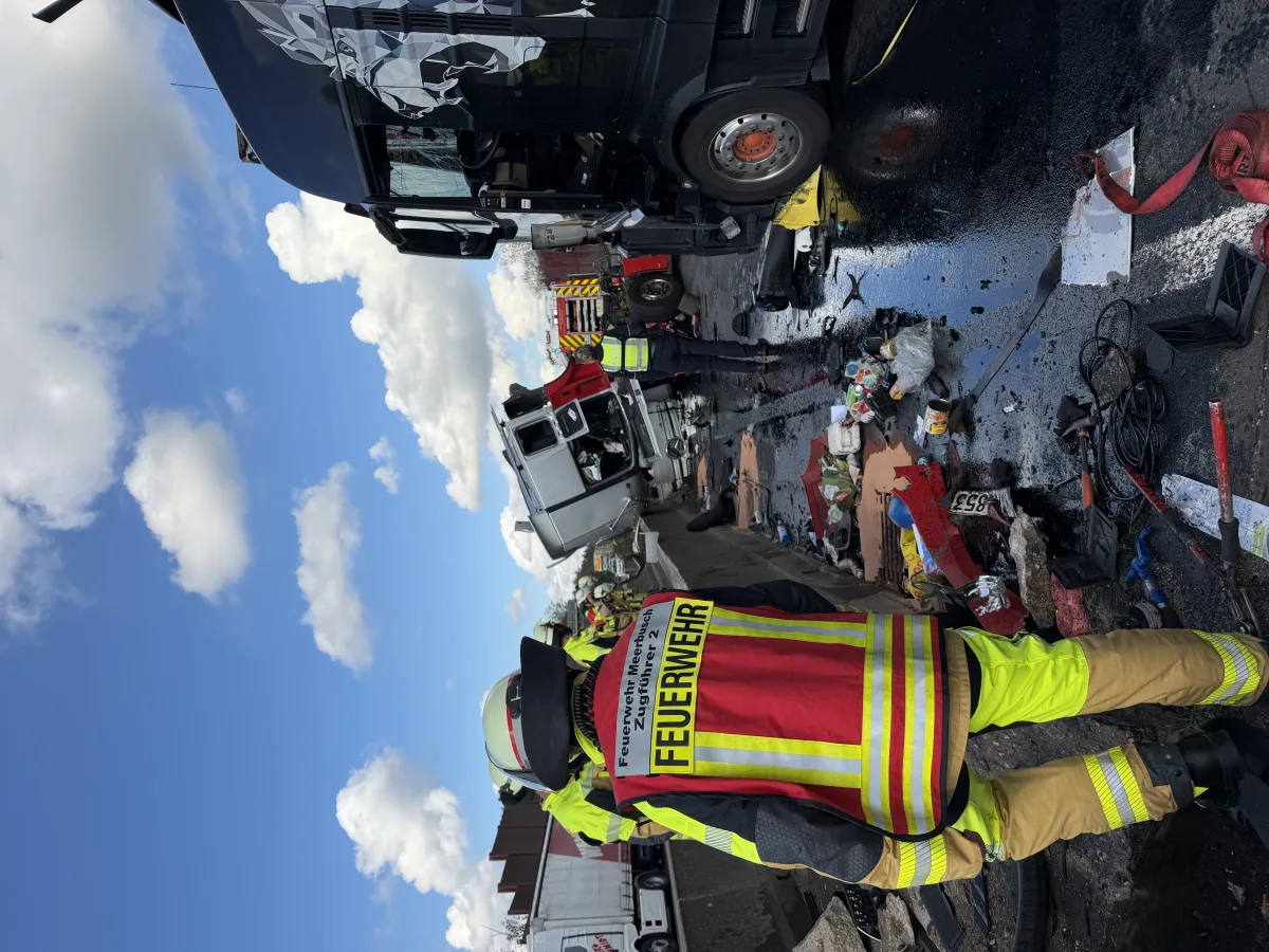 Mehrere Feuerwehrleute in Einsatzkleidung sichern die Unfallstelle mit einem umgestürzten Lkw ab, mit Trümmern auf der Straße.